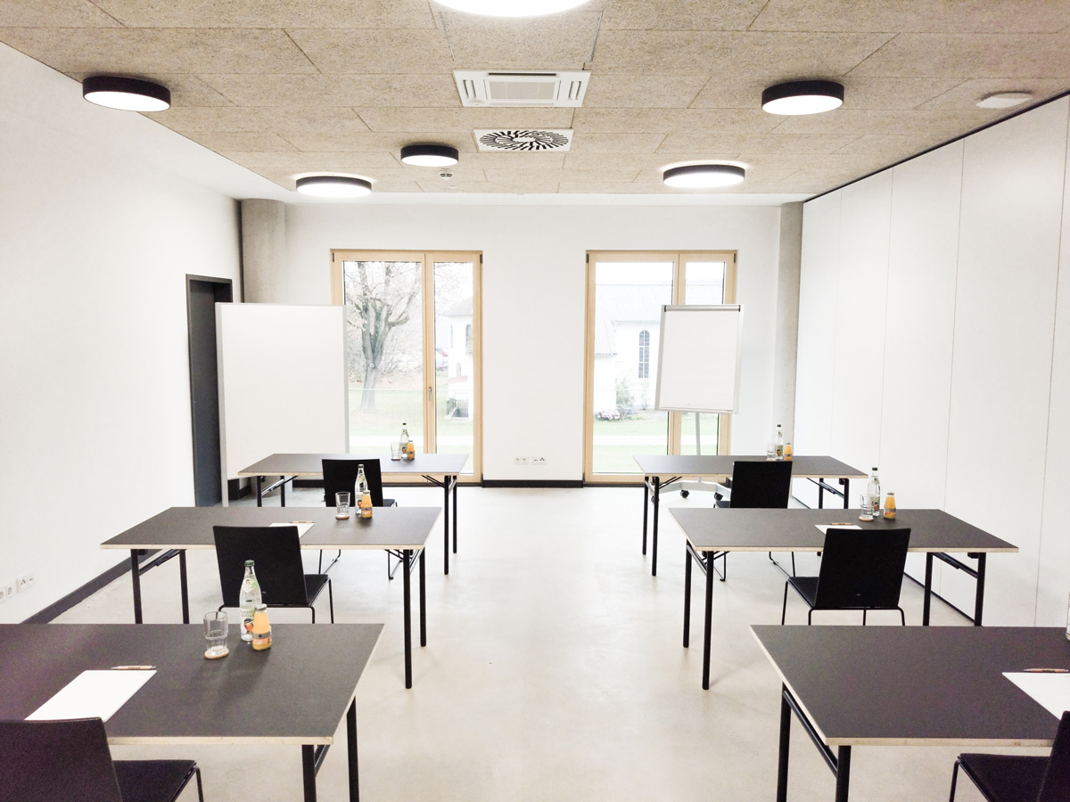 Seminarraum 3 – Prüfungsbestuhlung Arbeitsraum vor großen Fenstern mit Tischen und Stühlen