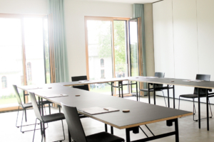 Arbeitsraum Schrägansicht Arbeitsraum zum Mieten in Augsburg mit großen Fenstern und Tischen und Stühlen.