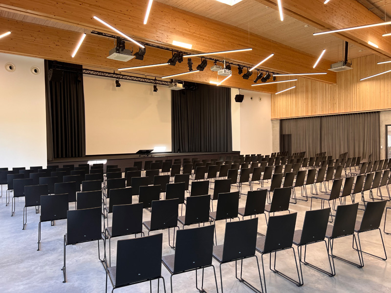 Veranstaltungssaal Schrägansicht Saal zum Mieten mit schwarzen Stühlen und großer Bühne